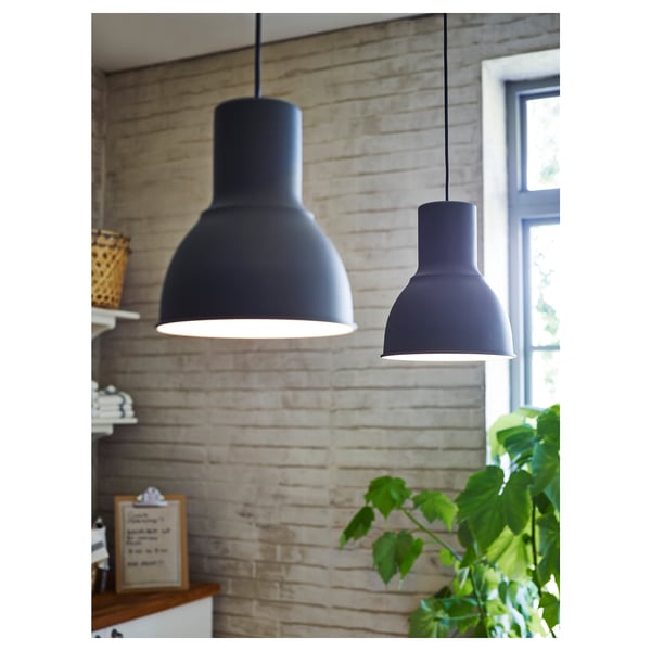 Two black pendant lamps illuminate wooden table against brick wall with greenery.