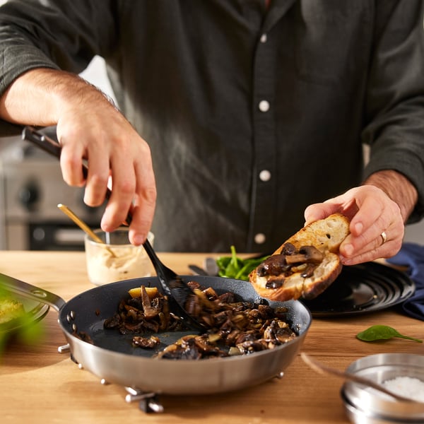 Cooking mushrooms in ceramic pan, using spatula and toast.