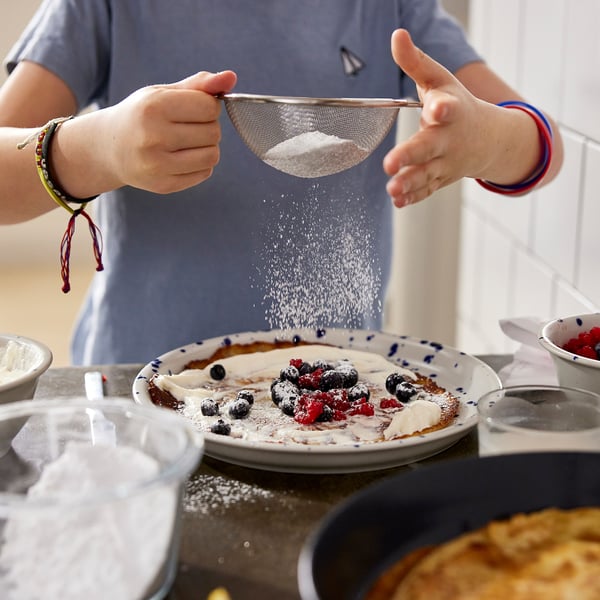 Sprinkling sugar on berry pancakes with kitchen tools nearby.