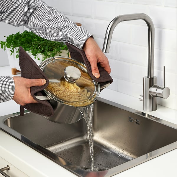 Person pours pasta into sink with glass lid strainer.