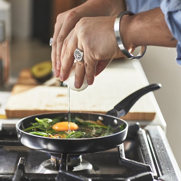 A person is cooking in a small, non-stick frying pan using an egg cracker, demonstrating the ease of use and non-stick feature on a stovetop.