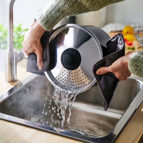 Person pours water from a pots with lid into a sink.