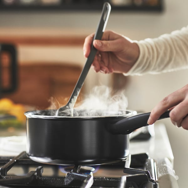 Person stirs food in a saucepan on a gas stove. The saucepan has steam vents and a comfortable grip handle.