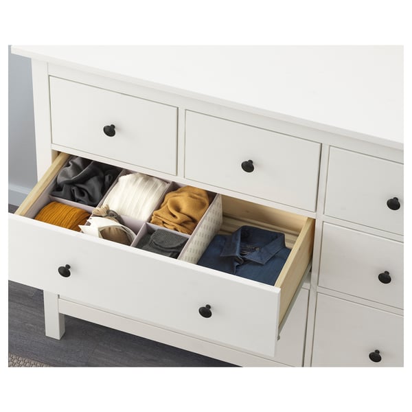 White chest of drawers with black knobs, showing organised clothes in three drawers. Part of IKEAs HEMNES bedroom furniture line.