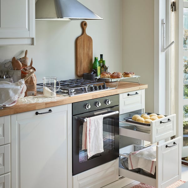 Kitchen with light countertop appliances, utensils, and a stove with exposed food on cooling rack.