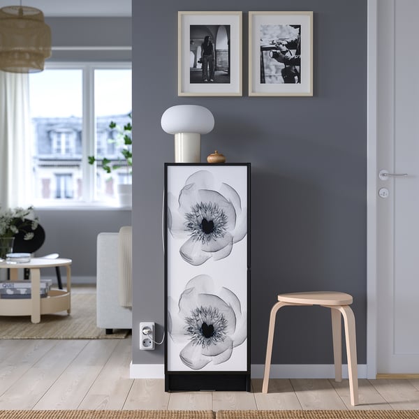Modern living room with HÖGBO cabinet, black & white flowers. White lamp, stool, city view, light wood floor, gray walls.