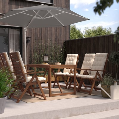 Outdoor seating with wooden table & HÖGÖN black parasol, cushioned chairs and lush plants, perfect for relaxation.