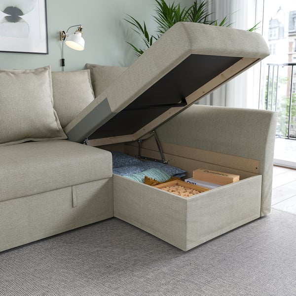 Beige sofa opens to reveal storage space under seat, holding pillows and blankets.