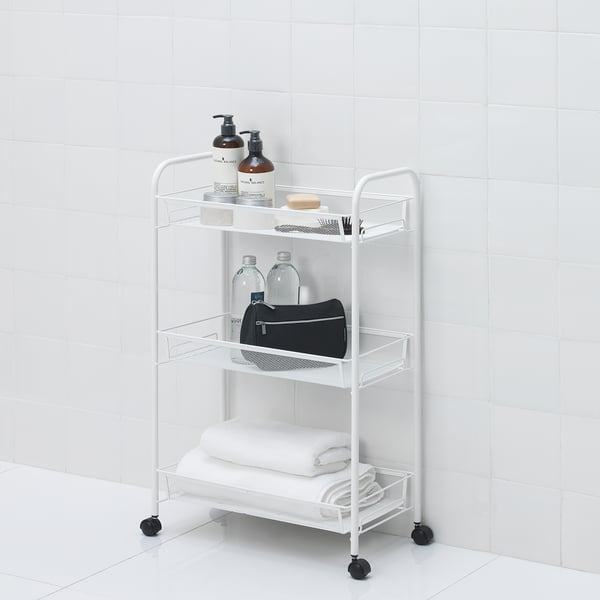 White mobile bathroom cart with three shelves holding towels, bottles, and toiletries. Easy to move with castor wheels.
