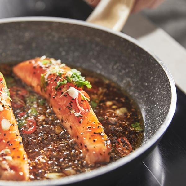 Black frying pan with salmon in dark sauce. Non-stick, even heat.