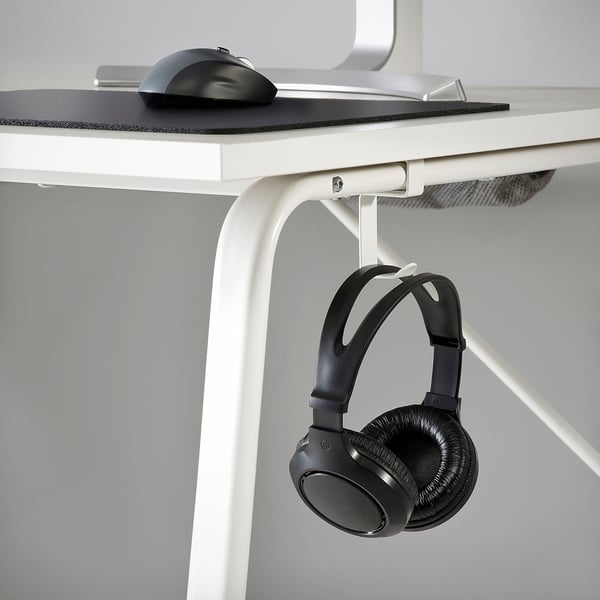A white gaming desk with a mouse pad and mouse on top. Underneath, a hook holds a pair of black headphones.