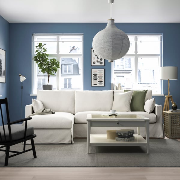 Stylish HYLTARP sectional sofa in blue-walled living room with storage chaise, large rug, pillows, lamp, and plant.