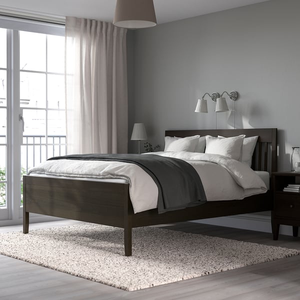 Modern grey bedroom: large bed centred, dark wood frame, white linens, bedside lamps, large window with curtains, light rug.