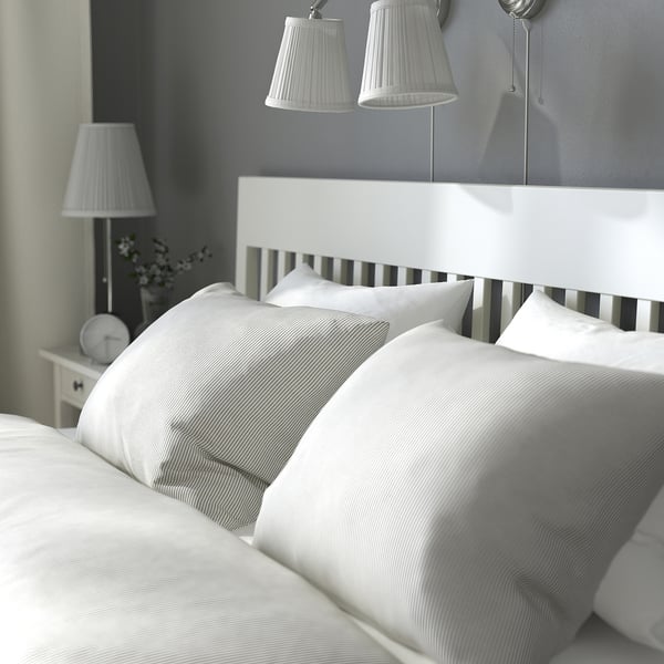 Bedroom scene with white IDANÄS bed, striped pillows, two table lamps, and wall-mounted lights. Clean, serene ambiance.
