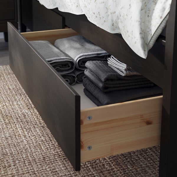Open drawer of dark wood bed storing folded grey towels and linens.
