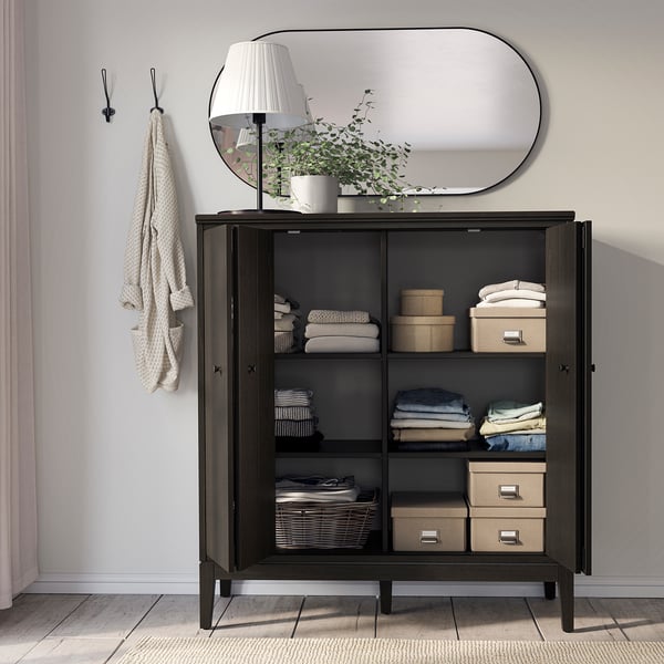 Modern dark wooden cabinet with mirrored top, featuring neatly folded clothes, boxes, and a lamp, ideal for storage and decor.