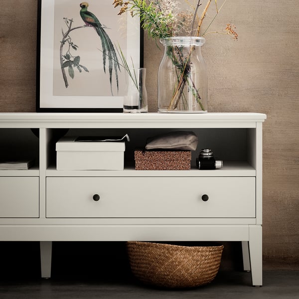 White tv console, IDANÄS series, with two drawers, open shelf, and woven basket underneath. Decorated with framed art, vases, and plants.
