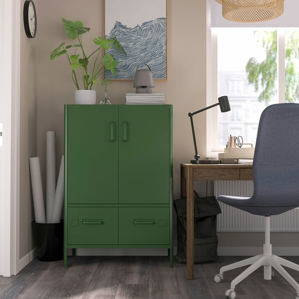 Modern office with green IDÅSEN cabinet, grey chair, wooden desk by window, plant, lamp, and artwork.
