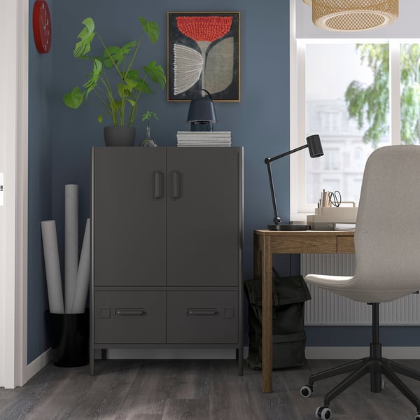 Modern home office with grey IDÅSEN cabinet, wooden desk, grey chair, blue wall, red clock, painting, black lamp, plant.