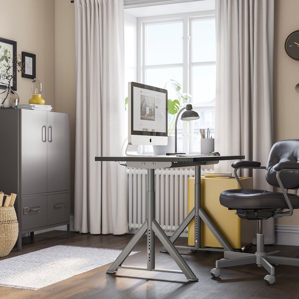 Modern home office with IDÅSEN desk, adjustable height, computer setup, swivel chair, large window, storage cabinet, lamp, and decor.