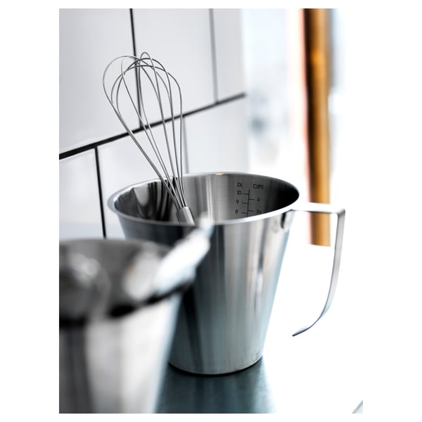 Stainless steel measuring jug with handle, containing a whisk. Ideal for kitchen tasks.