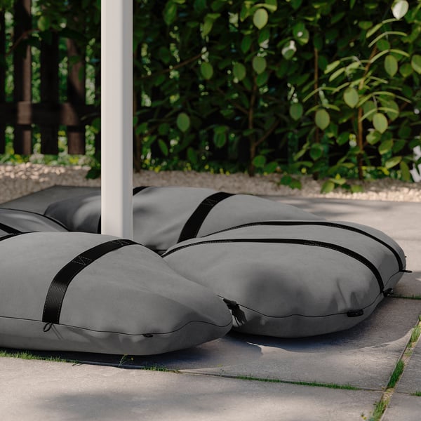 Four grey IGGÖN sandbags with black straps for parasol stability on concrete.