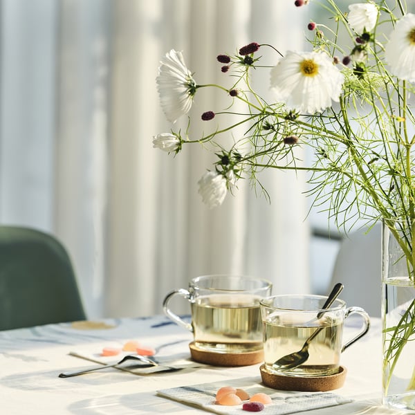Table set with white flowers, two mugs, and coasters. The coasters help protect the tabletop and minimise noise from cups.