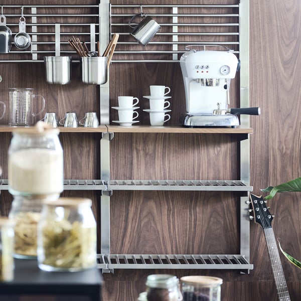 Wooden shelves display an espresso machine, stacked white cups, and jars. A guitar leans against the wall.