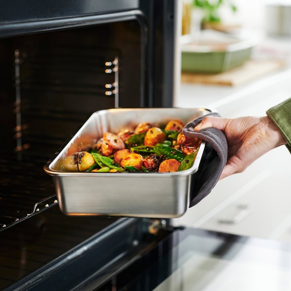 Person pulls out metal tray with cooked vegetables from oven.