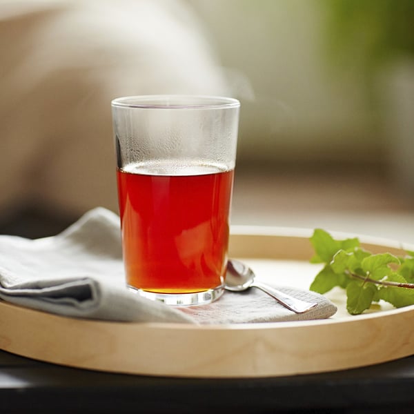 A clear glass of red juice on a wooden tray with a spoon and mint leaf, part of IKEAs practical and stylish glassware series.