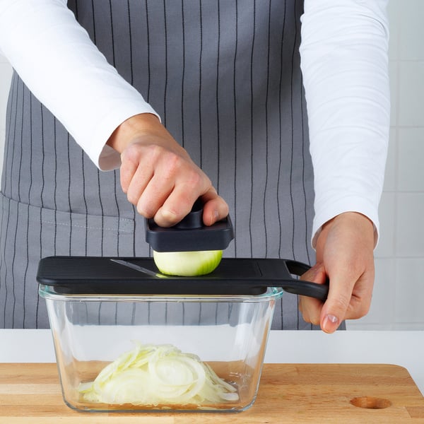 Person uses mandoline slicer, adjusting thickness dial, slicing onion, storing slices in glass container.