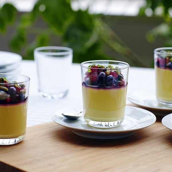 Glasses with creamy dessert and berries on white plates on wooden table.