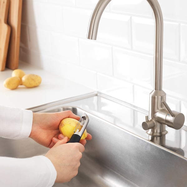 Person peeling potato near sink with IKEA peeler.