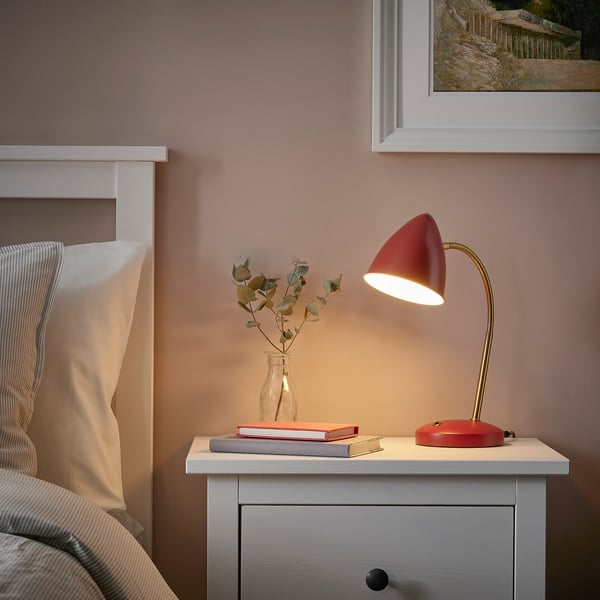 Red ISNÅLEN lamp on bedside table, illuminated with book and flowers, adding retro charm to bedroom.