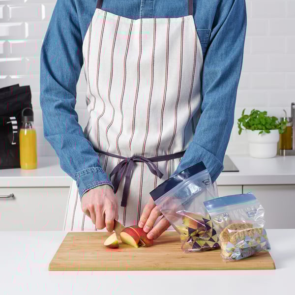 A person in an apron chops an apple on a cutting board, using resealable ikea bags to store pieces.