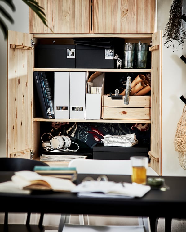 Organised wooden IVAR cabinet with books, boxes, and headphones in a home office. Wooden finish, rectangular shape, practical design.