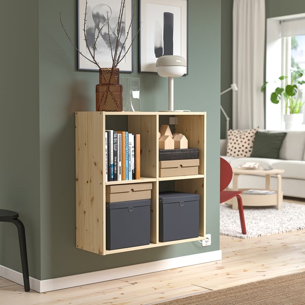 Light wood IVAR bookshelf against green wall, holding boxes & books, smaller than wall art and couch.