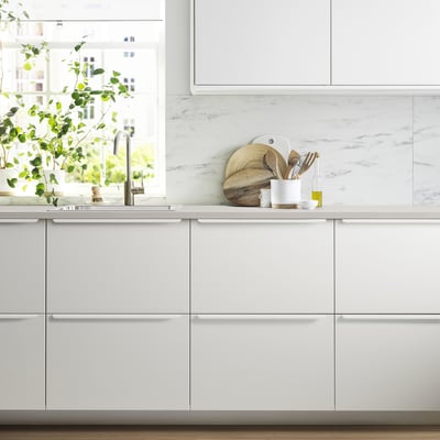 Modern white kitchen: JÄRSTORP countertop, marble backsplash, wooden utensils, potted plant. Sink & tap visible.