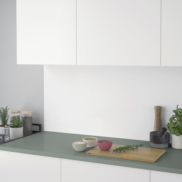 Modern kitchen counter with green worktop, bowls, wooden board, and potted plants.