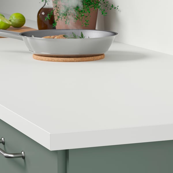 A modern kitchen counter with a white JÄRSTORP laminate worktop displaying a frying pan, easy to clean and durable.