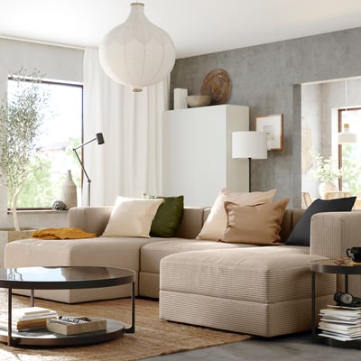 Modern living area with beige JÄTTEBO modular sofa, cushions, round coffee table, lamp, and rug under large window.