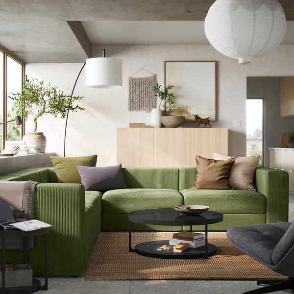 Bright living room with green corduroy JÄTTEBO sofa, natural wood cabinet, large plants, textured rug, hanging lamps, and modern decor.