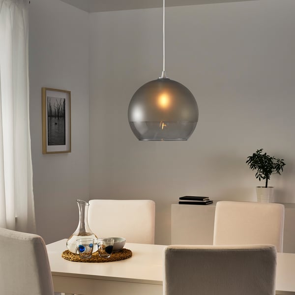 Modern dining area with glass pendant lamp over white table and beige chairs, tray with pitcher and glasses.