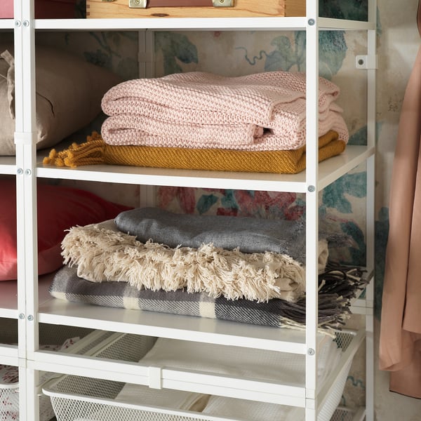 White JONAXEL storage shelving unit with folded pink, yellow, grey, and striped blankets neatly organised.