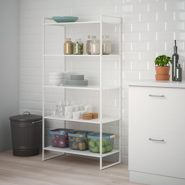 White JONAXEL storage unit in kitchen corner, holding plates, jars, and fruit baskets.