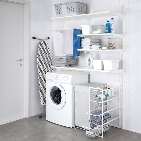 Neat laundry room with white JONAXEL storage. Shelves hold folded towels, baskets, & cleaning supplies. Washer below, ironing board leaning.
