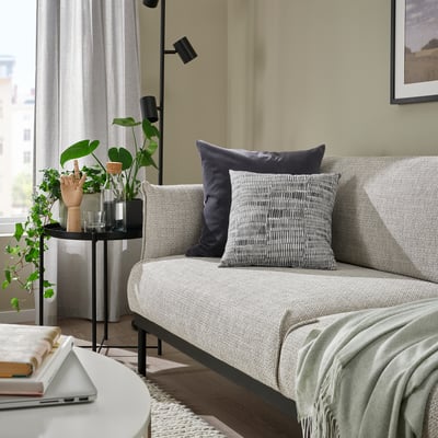 Living room with grey JORDKASTANJ cushion, laptop, books, plant, and minimalist decor.