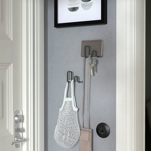 Wall hooks holding keys, bag, and wallet next to door.