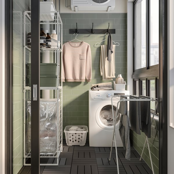Organised laundry room with JOSTEIN storage. Washing machine, hooks, green tiled wall, and storage baskets.