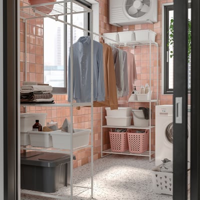 Highly organised laundry room with JOSTEIN storage: white shelves, pinkish tiles, clothes on hangers, washing machine, baskets, bottles, clear window.